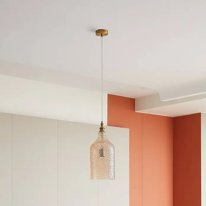 Lindby Pendelleuchte Drakar - creme / amber, amber, gold, E27 - Strukturierte bernsteinfarbene Glas-Pendelleuchte mit Messingakzenten hängt von der Decke in einem modernen Raum.