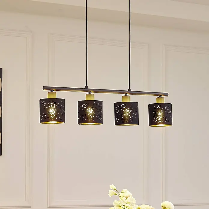 Lindby Pendelleuchte Vasilia - L x B x H: 75 x 12 x 11 cm, schwarz, Schwarz, gold, E14 - Vierflammige Pendelleuchte mit schwarzen Schirmen, Sternenperforationen, goldener Innenseite und dunkler Metallstange über einem Tisch.