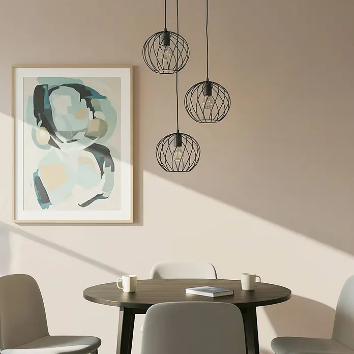 Lindby Pendelleuchte Danika - schwarz, Schwarz, E27 - Drei schwarze Pendelleuchten mit Drahtkäfig illuminieren einen Essbereich mit Rundtisch, Stühlen und abstrakter Wandkunst.
