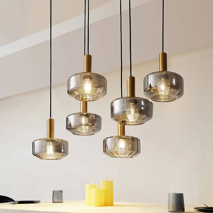 Lindby Pendelleuchte Hildur - alu / grau / zink, rauchgrau, messing, E27 - Moderne Pendelleuchten mit Rauchglas-Schirmen und Messingakzenten beleuchten einen Tisch.