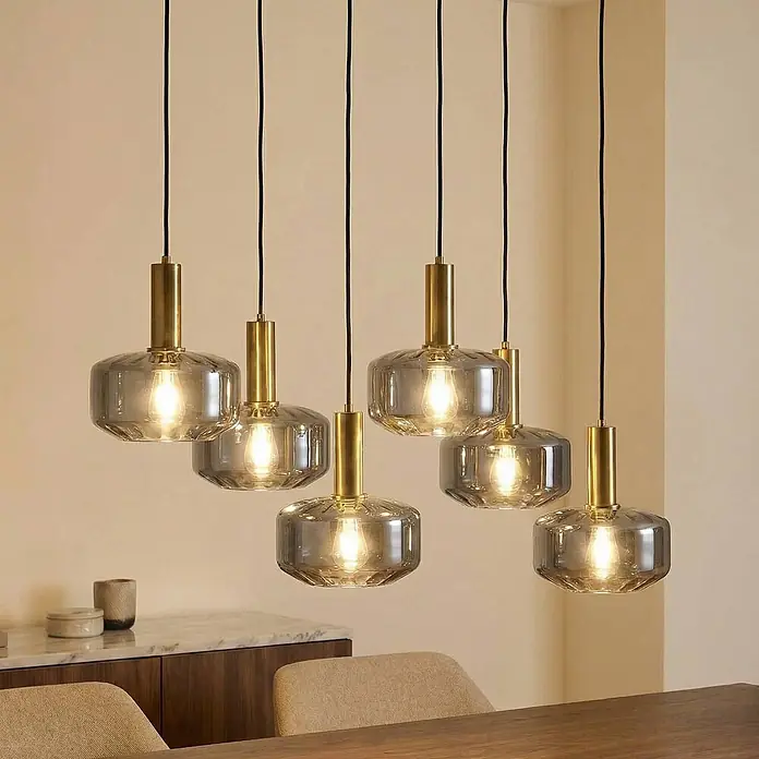 Lindby Pendelleuchte Hildur - alu / grau / zink, rauchgrau, messing, E27 - Sechs moderne Pendelleuchten aus Rauchglas und Messing erhellen einen Essbereich.
