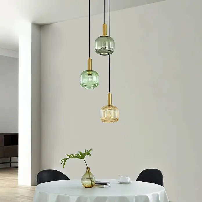 Lindby Pendelleuchte Dorotoe - L x B x H: 45 x 45 x 18 cm, Multicolour, Grün, amber, rauchgrau, E27 - Drei elegante Pendelleuchten mit gerippten Glasschirmen (zwei grün, eine bernsteinfarben) und messingfarbenen Akzenten hängen über einem Esstisch.
