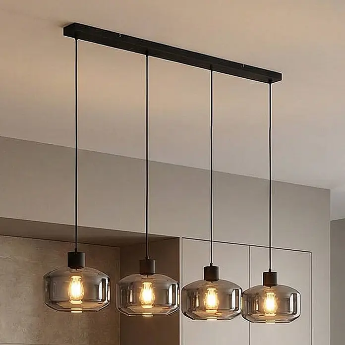 Lindby Pendelleuchte in rauchgrau transparent, schwarz matt, Hängelampe -  - Lineare Pendelleuchte mit vier Rauchglas-Schirmen und sichtbaren Glühbirnen, die an einer schwarzen Deckenleiste hängt.