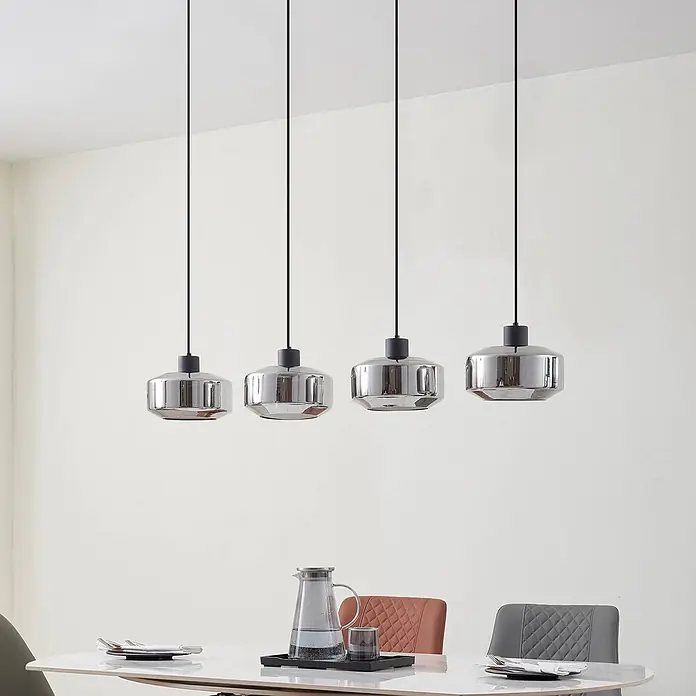 Lindby Pendelleuchte in rauchgrau transparent, schwarz matt, Hängelampe -  - Vier moderne, silberfarbene Pendelleuchten hängen in einer Reihe über einem Esstisch.