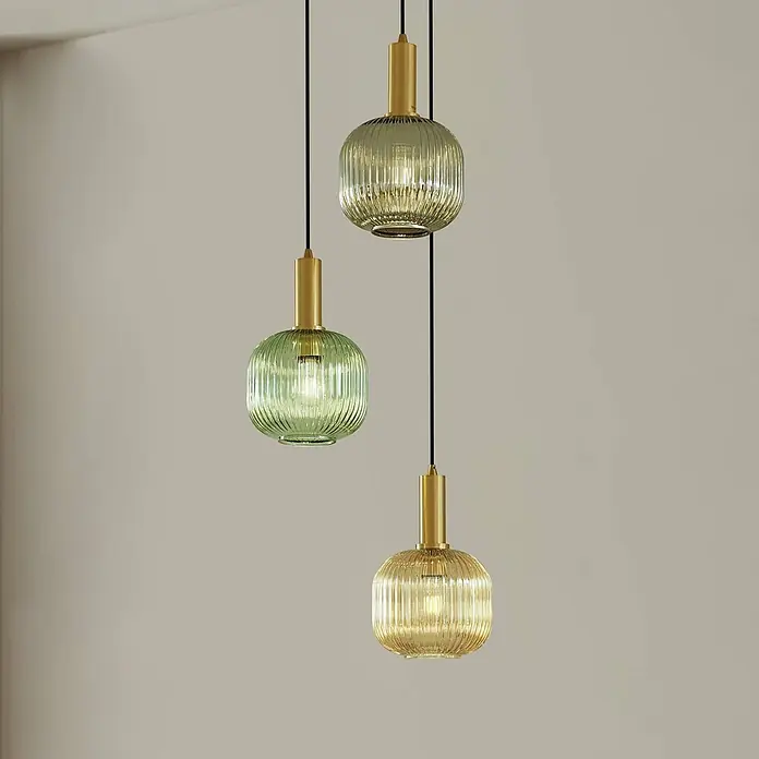 Lindby Pendelleuchte Dorotoe - L x B x H: 45 x 45 x 18 cm, Multicolour, Grün, amber, rauchgrau, E27 - Drei gerippte Pendelleuchten aus Glas (zwei grün, eine bernsteinfarben) mit goldfarbenen Metalldetails, hängend und beleuchtet.
