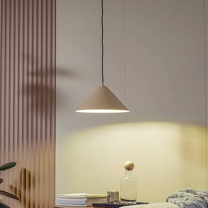 Lindby Pendelleuchte Clarine - creme / amber, beige, E27 - Eine beige konische Pendelleuchte beleuchtet einen Nachttischbereich mit warmem Licht.