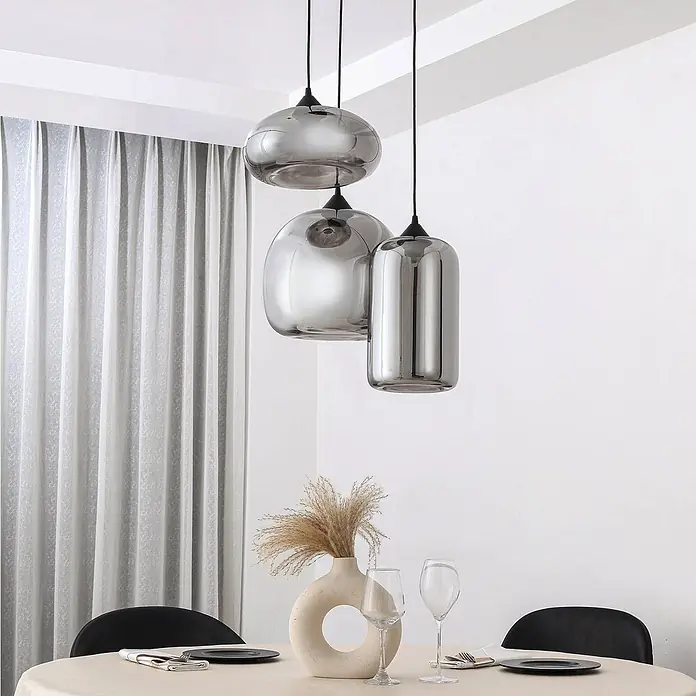 Lindby Pendelleuchte Marla - L x B x H: 50 x 50 x 30 cm, schwarz, Schwarz, rauchgrau, E27 - Drei Pendelleuchten aus Rauchglas in verschiedenen Formen hängen über einem gedeckten Esstisch.