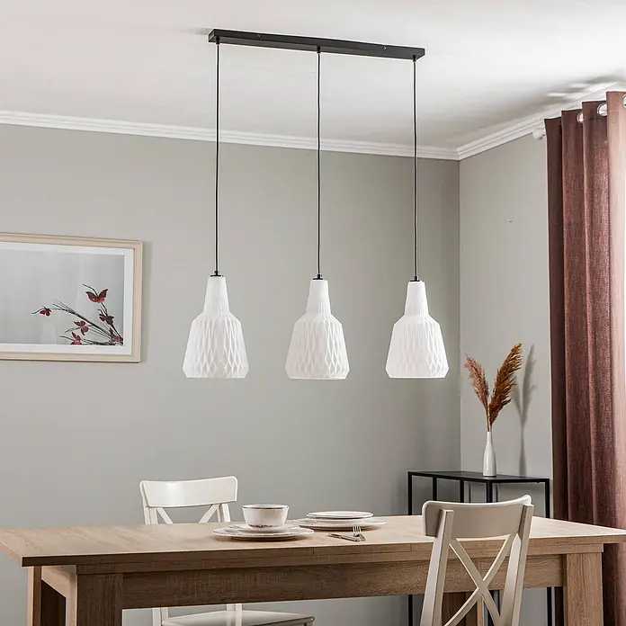 Lindby Pendelleuchte Belarion - L x B x H: 98 x 23 x 35 cm, weiß / opal, opal, E27 - Drei weiße, texturierte Pendelleuchten hängen an einer schwarzen Leiste über einem Holztisch.