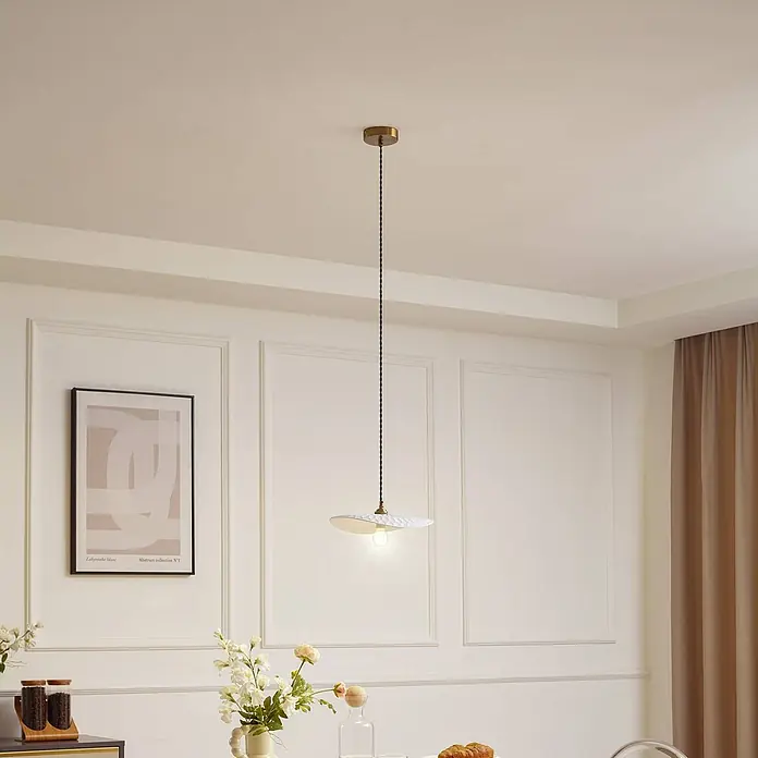 Lindby Pendelleuchte Annira - weiß / opal, weiß, messing, E14 - Eine weiße, strukturierte Pendelleuchte mit Messingakzent und schwarzem Zopfkabel hängt von der Decke und beleuchtet einen modernen Raum.
