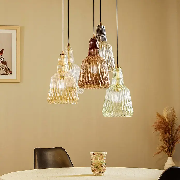 Lindby Pendelleuchte Belarion - L x B x H: 65 x 65 x 35 cm, Multicolour, bernstein, rauchgrau, hellGrün, transparent, Kupfer, E27 - Eine Gruppe bunter, facettierter Glas-Pendelleuchten hängt über einem Esstisch.
