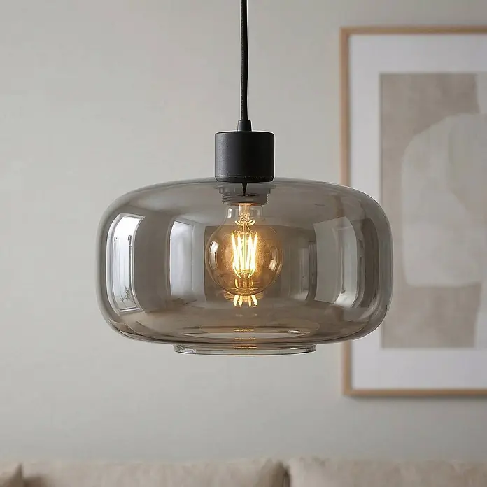 Lindby Pendelleuchte Hildur - L x B x H: 28,5 x 28,5 x 14,5 cm, alu / grau / zink, rauchgrau, sandSchwarz, E27 - Eine Pendelleuchte aus Rauchglas mit schwarzer Fassung hängt und leuchtet warm.