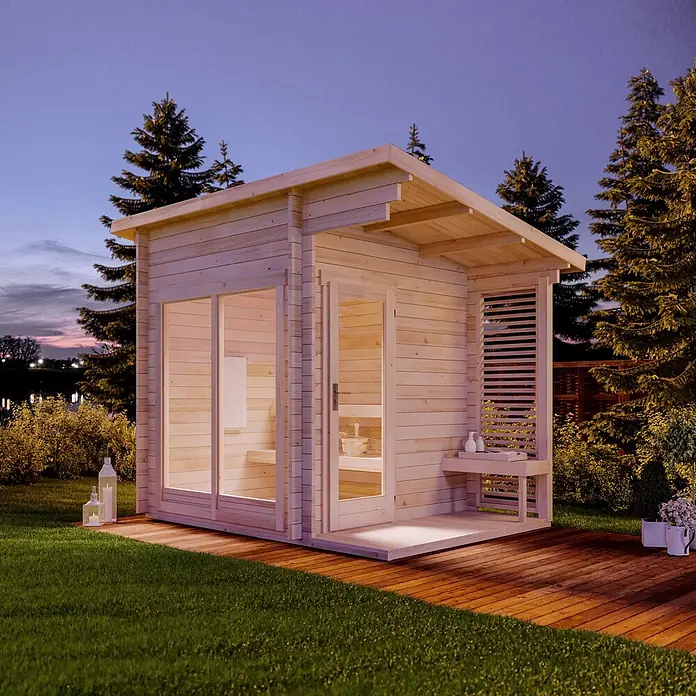 FinnTherm Saunahaus Lizzy S - L x B x H: 251 x 33 x 262 cm - Helle Holzgarten-Saunakabine mit Glasfront, beleuchtetem Innenraum und Holzterrasse im Garten bei Dämmerung.