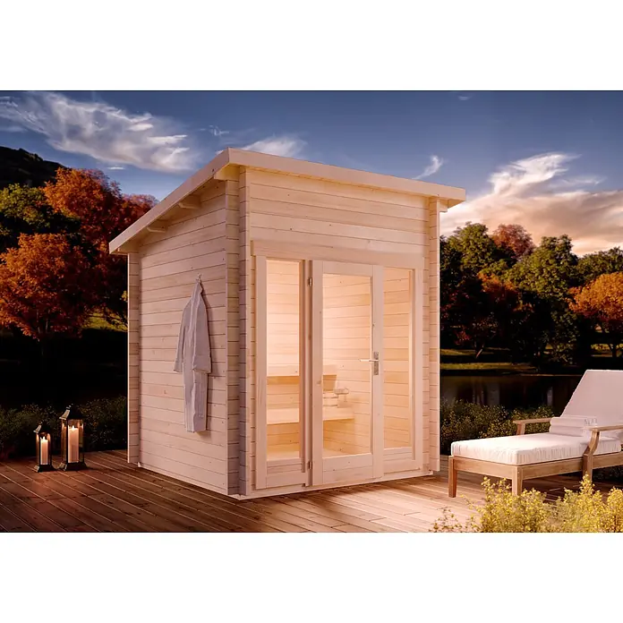 FinnTherm Saunahaus Lizzy XS 40mm Wandstärke -  - Helle Holz-Außensaunakabine auf einer Terrasse, mit beleuchtetem Innenraum und Bademantel draußen, am See in der Dämmerung.