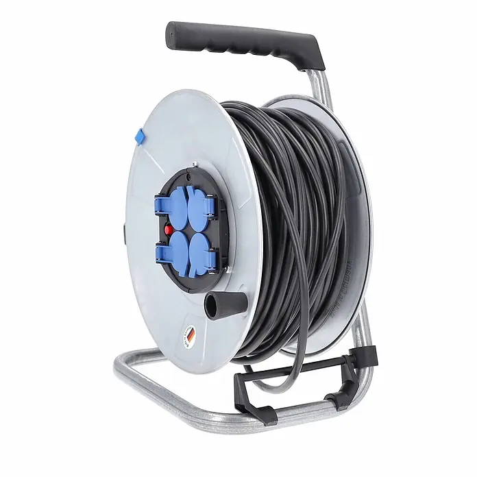 as - Schwabe Metallkabeltrommel 50m H05VV-F 3G1,5 IP20 -  - Graue Kabeltrommel mit schwarzem Kabel, vier blauen Steckdosen und schwarzem Griff auf silbernem Metallrahmen.