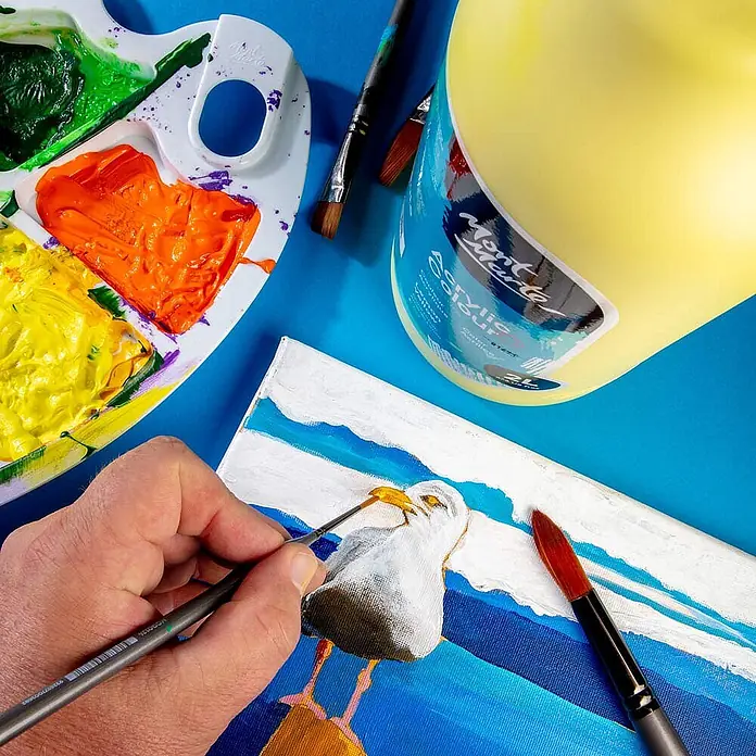 Mont Marte Acrylfarbe Signature - Zitronengelb, 2.000 ml, Flasche mit Tropfpipette - Person malt Seemöwe auf Leinwand mit gelber Mont Marte Acrylfarbe aus großer Flasche, neben Palette und Pinseln.