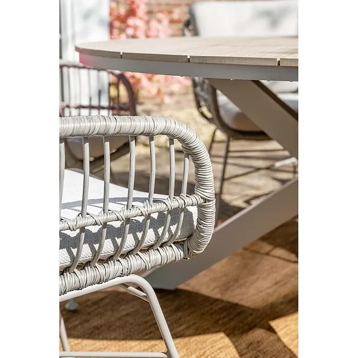 Garden Impressions Gartensessel Margriet - 1 Stk., Stahl, Polyester, Stapelbar, Taupe/Sand, B x T x H: 69,5 x 91 x 59 cm - Outdoor-Stuhl aus hellgrauem Rattan mit weißem Kissen, neben einem Tisch mit Holzoptik-Platte.