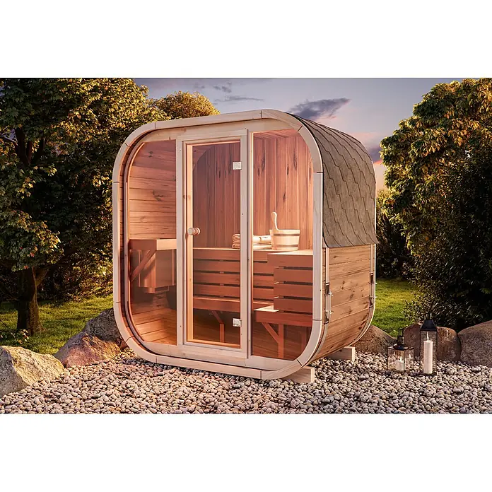 FinnTherm Fasssauna Ellipso M - Holz, L x B x H: 113 x 195 x 210 cm - Hölzerne Fasssauna mit Glastür und Schindeldach, draußen auf einer Kiesterrasse zwischen Bäumen.