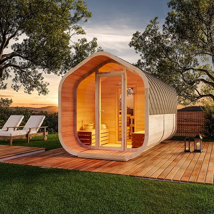 FinnTherm Fasssauna ScandiCube Wave Deluxe - Holz, L x B x H: 406 x 237 x 249 cm - Moderne Holz-Gartensauna mit dunklem Dach, von innen beleuchtet, auf einer Terrasse bei Sonnenuntergang.