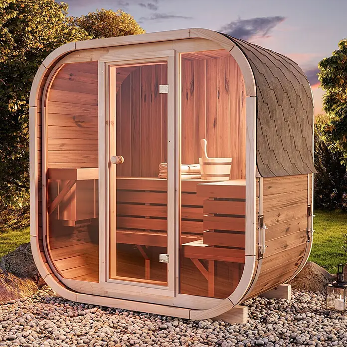 FinnTherm Fasssauna Ellipso M - Holz, L x B x H: 113 x 195 x 210 cm - Eine Holzfasssauna mit Glastür, Schindeldach und Innenbänken, im Freien auf Kies bei Sonnenuntergang.