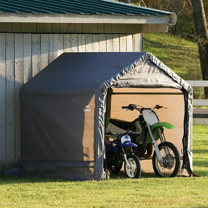 ShelterLogic Gerätehaus - Außenbreite inkl. Dachüberstand: 180 cm, Außentiefe inkl. Dachüberstand: 196 cm, Stahl, Grau - Ein graues ShelterLogic-Zelt beherbergt zwei Motorräder auf einer grünen Rasenfläche, die Schutz und Lagerraum bietet.
