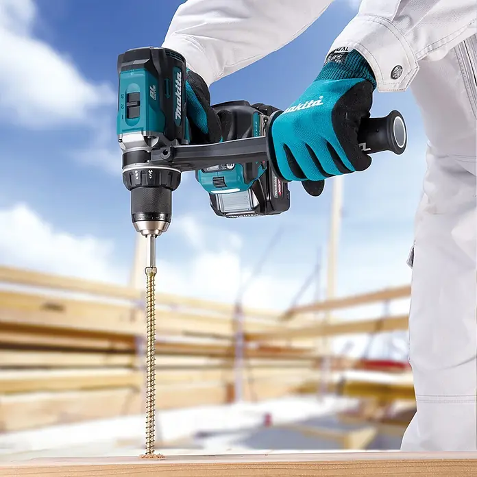 Makita XGT 40V max. Akku-Bohrschrauber DF003G - 40 V, Ohne Akku, 150 Nm - Eine Person in Arbeitshandschuhen bedient einen blau-schwarzen Makita Bohrschrauber, um eine lange Goldschraube in ein Holzbrett zu drehen.