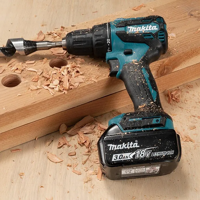 Makita LXT 18V Akku-Bohrschrauber DDF490Z - 18 V, Ohne Akku, 50 Nm - Türkise und schwarze Makita Akku-Bohrmaschine mit großem Holzbohrer, bedeckt mit Holzspänen auf einer Holzoberfläche mit zwei Bohrlöchern.