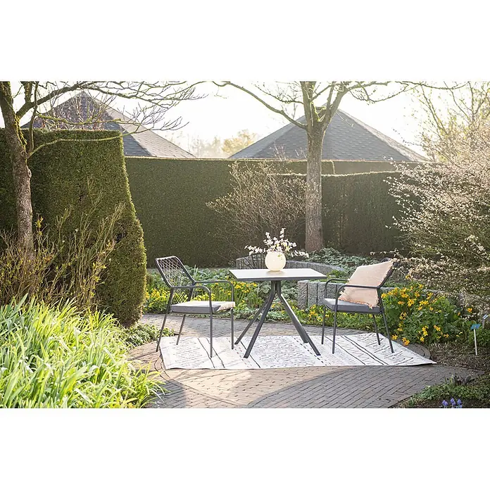Garden Impressions Gartensessel Dido - 1 Stk., Stahl, Polyester, Stapelbar, Schwarz/Grau, B x T x H: 63 x 85 x 55 cm - Dunkelgrauer Metall-Gartentisch und zwei Stühle mit hellgrauen Kissen auf einem gemusterten Teppich in einem sonnigen Garten.