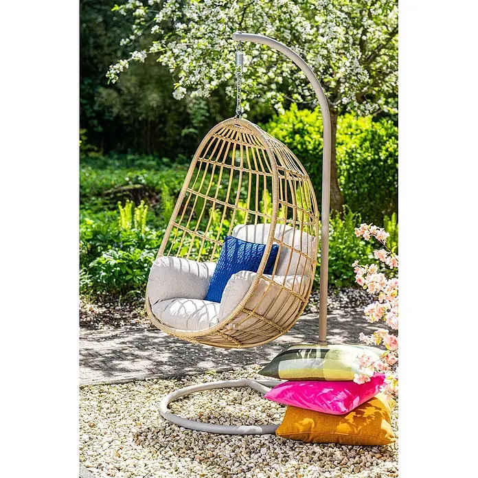 Garden Impressions Hängesessel Fargo - L x B x H: 92 x 79 x 198 cm, Metall, Beige - Ein naturfarbener Rattan-Hängekorbsessel mit hellgrauen Polstern und blauem Kissen, an einem grauen Gestell in einem sonnigen Garten.