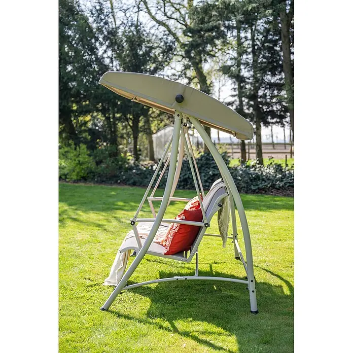 Garden Impressions Hollywoodschaukel Rubens - Aluminium, Max. Personenzahl: 3 Stk., Taupe - Eine Gartenschaukel mit beigem Dach und grauer Sitzfläche, ausgestattet mit einem orangefarbenen Kissen, steht in einem sonnigen Garten.