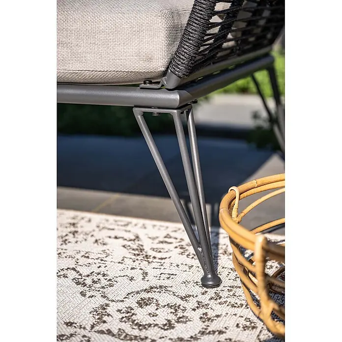 Garden Impressions Loungesofa - B x T x H: 97 x 175 x 73 cm, Aluminium, Polyester, Schwarz/Sand - Nahaufnahme eines dunkelgrauen Metall-Gartenstuhls mit hellem Kissen und geflochtener Rückenlehne, auf einem gemusterten Teppich neben einem Weidenkorb.