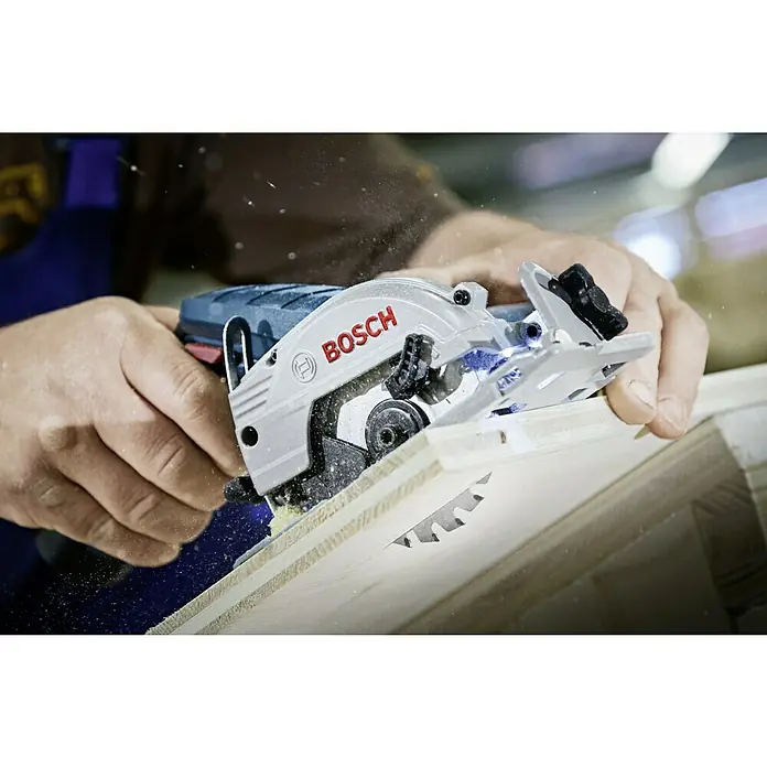 Bosch Professional Akku-Handkreissäge GKS 12V-26 L-Boxx - 12 V, Ohne Akku, Sägeblatt: 85 mm, Leerlaufdrehzahl: 1.400 U/min - Eine Bosch-Kreissäge schneidet präzise ein Holzbrett, wobei die Sägespäne deutlich sichtbar sind, was die Leistung des Werkzeugs hervorhebt.