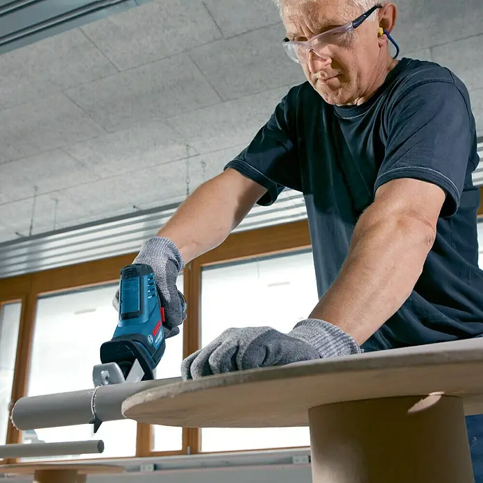 Bosch Professional Akku-Säbelsäge GSA 12V-14 - 12 V, Li-Ionen, Ohne Akku, Leerlaufhubzahl: 0 /min - 3.000 /min - Ein Mann schneidet mit einer Bosch Akku-Säbelsäge ein Rohr. Er trägt Schutzbrille und Handschuhe für die Arbeitssicherheit.