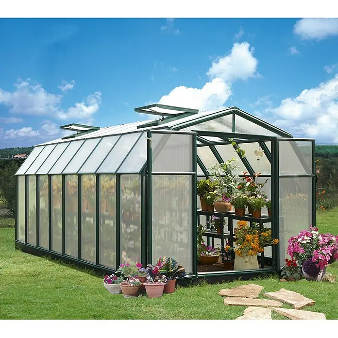 Palram – Canopia Invernadero Hobby Gardener - Medidas ext. (An x Pr): 266 x 516 cm, 6 mm, Verde - Un gran invernadero con plantas y flores dentro y fuera, con un telón de fondo de cielo azul despejado.