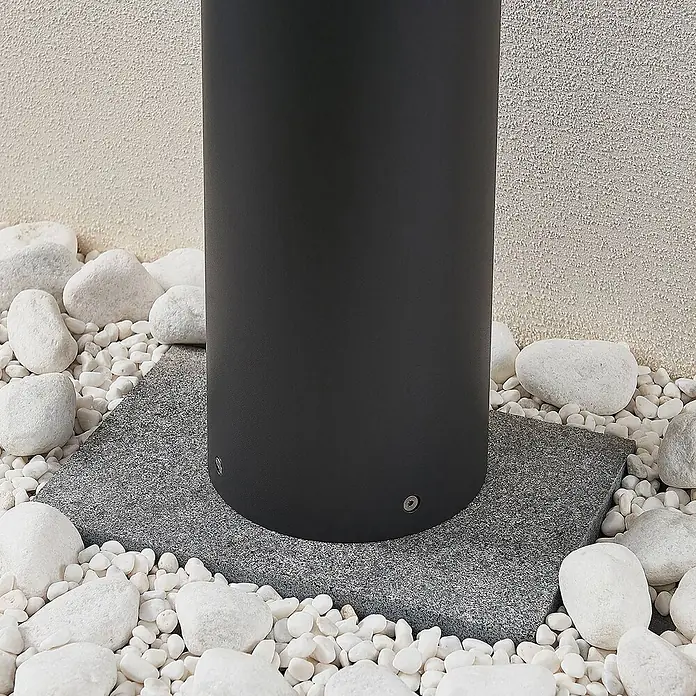 Lucande Außenlaterne Darja -  - Matter schwarzer zylindrischer Pfostenfuß auf grauer Granitplatte, umgeben von weißen Kieselsteinen.