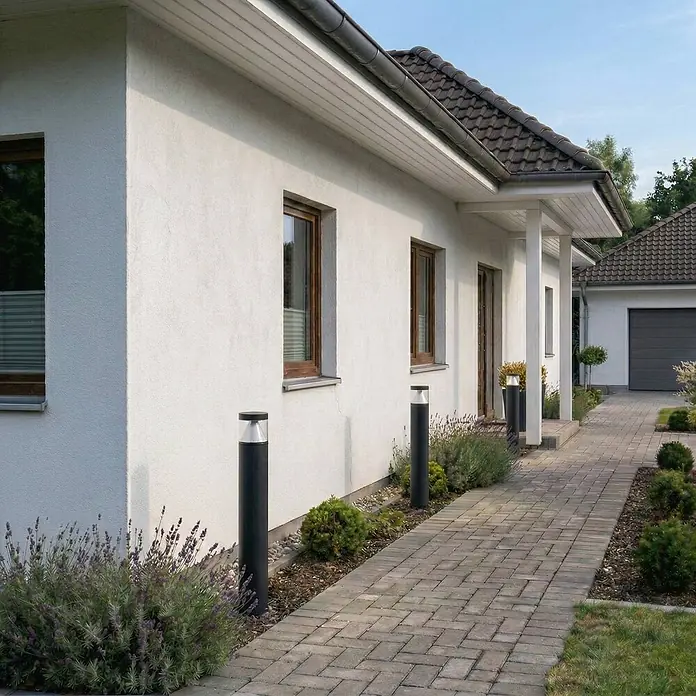Lucande Außenlaterne Darja -  - Schwarze zylindrische Pollerleuchten beleuchten einen gepflasterten Weg neben einem Haus.