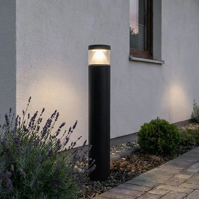 Lucande Außenlaterne Darja -  - Schwarze Außenpollerleuchte beleuchtet einen Weg neben einem Haus, umgeben von Lavendel.