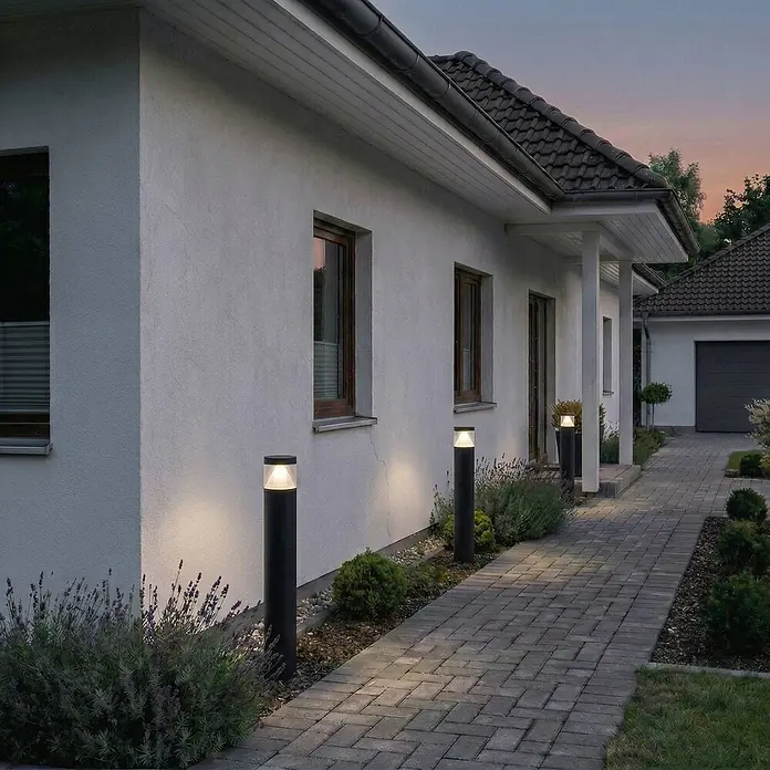 Lucande Außenlaterne Darja -  - Drei schwarze Wegeleuchten erhellen einen gepflasterten Gehweg neben einem Haus in der Dämmerung.