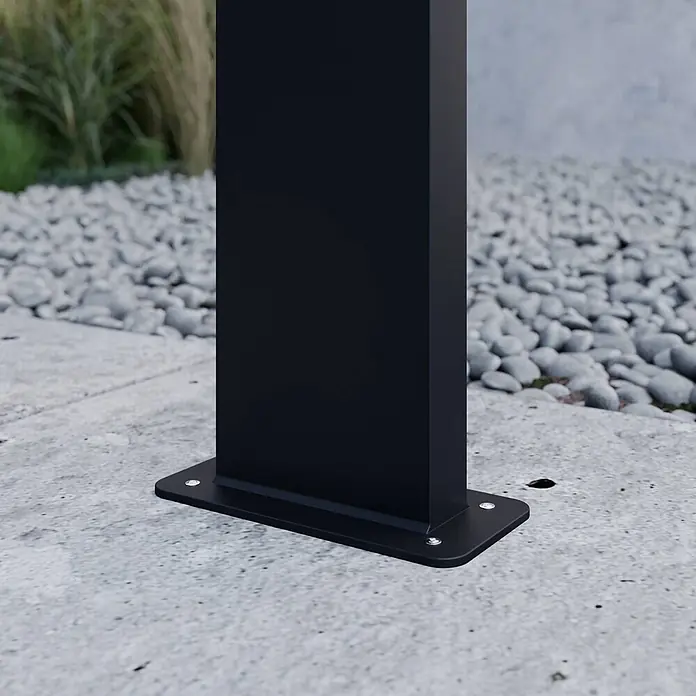 Lucande Außenlaterne Nevio -  - Schwarze Metallpfostenbasis sicher auf Betonboden verankert, mit Kies und Grün im Hintergrund.