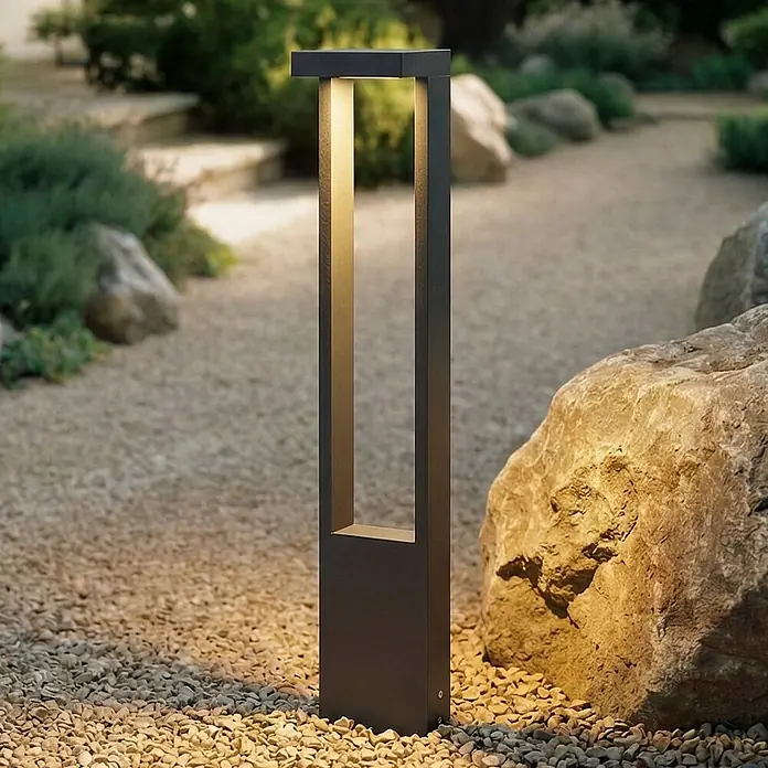 Lindby Außenlaterne Lonete - 10 x 12 x 65 cm - Moderne, dunkelgraue Pollerleuchte mit warmer Beleuchtung, die einen Kiesweg im Garten akzentuiert.