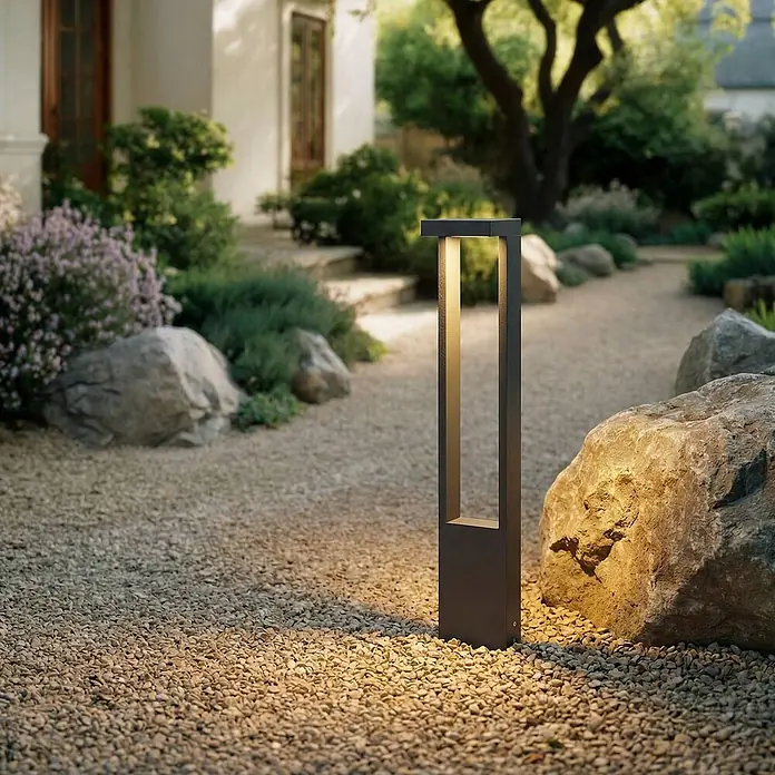 Lindby Außenlaterne Lonete - 10 x 12 x 65 cm - Modernes anthrazitfarbenes Wegeleuchte erhellt einen Kiesweg im Garten mit warmem Licht.