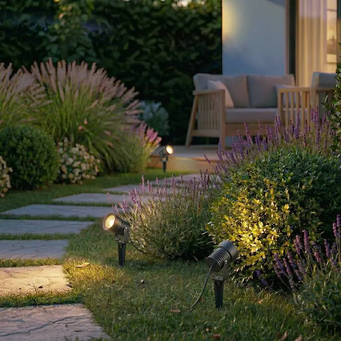 Lucande Erdspießleuchte Irina -  - Dunkelgraue Metall-Gartenspots beleuchten einen Gartenweg, Büsche und Lavendel bei Nacht.