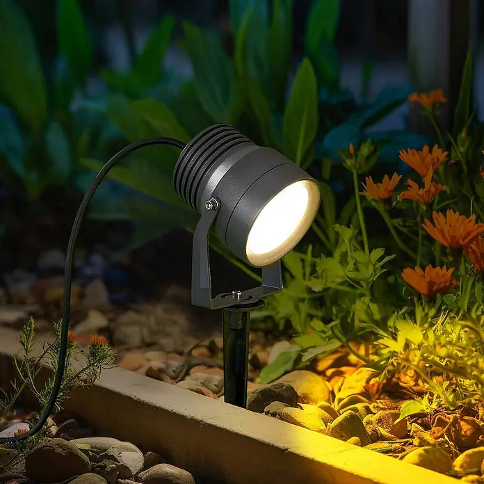 Lucande Erdspießleuchte Irina -  - Dunkelgrauer Outdoor-Strahler beleuchtet orangefarbene Blumen und Gartensteine. Die Metall-Erdspießleuchte spendet hellweißes Licht.