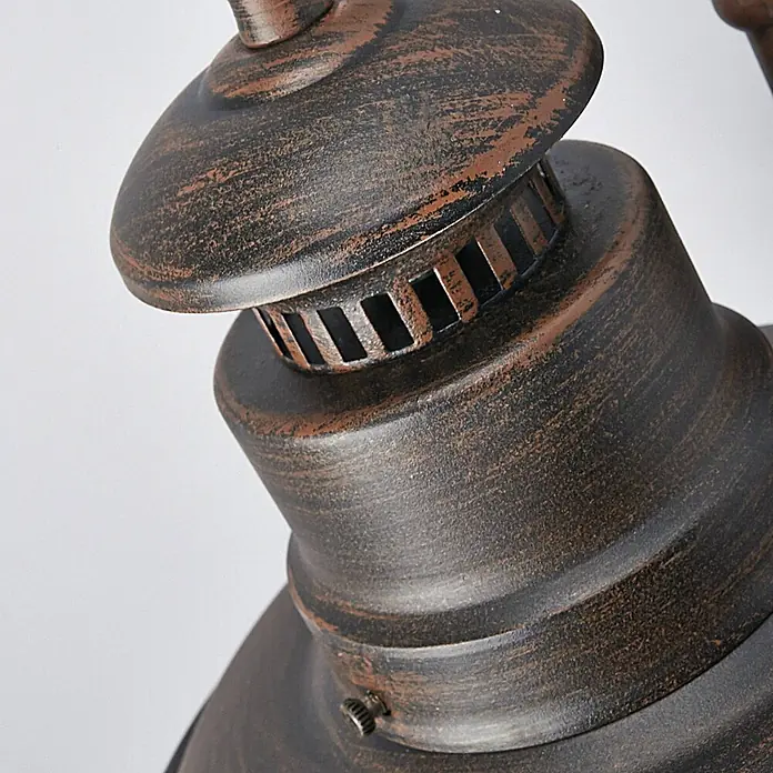 Lindby Außenwandleuchte Eddie - braun / rost, IP44 - Nahaufnahme eines verwitterten Bronze- und Schwarzmetall-Leuchtenbauteils mit Lüftungsschlitzen.
