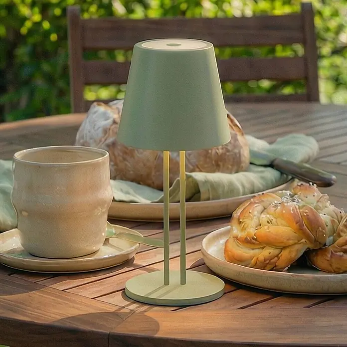 Lindby Tischleuchte Janea - L x B x H: 11,4 x 11,4 x 25 cm, grün, grün - Kompakte, salbeigrüne tragbare Tischlampe auf einem hölzernen Gartentisch mit Speisen.