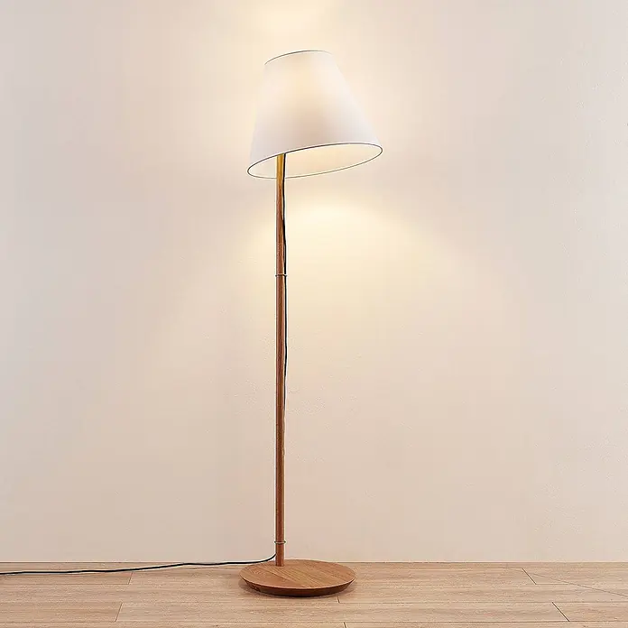Lucande Stehleuchte Jinda - Höhe: 160 cm, Holz dunkel, weiß / opal, E27 - Große Stehlampe mit Holzständer und weißem Stoffschirm, die warmes Licht auf eine helle Wand und einen Holzfußboden wirft.