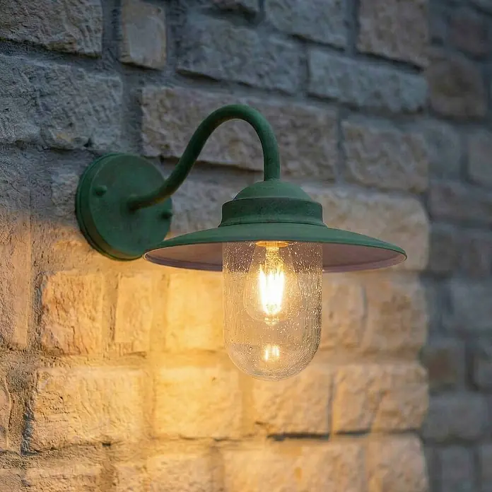 Lindby Außenwandleuchte Bilma - grün, IP44 - Grün patinierte Außenwandleuchte mit strukturiertem Glasschirm und warmer Glühbirne, an Steinwand montiert.