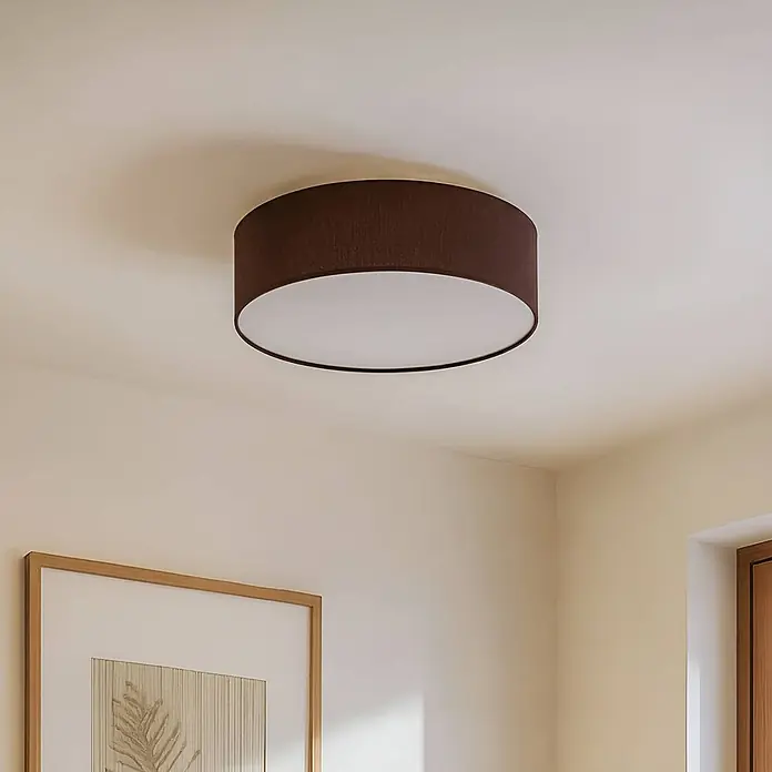 Lindby Deckenleuchte Sebatin - L x B x H: 40 x 40 x 17 cm, braun / rost, E27 - Runde, dunkelbraune Stoff-Deckenleuchte mit weißem Diffusor, montiert an einer cremefarbenen Decke.