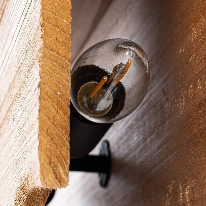 Lucande Wandleuchte Tarry - Holz hell, E14 - Eine klare LED-Glühbirne mit orangefarbenen Filamenten an einer schwarzen Halterung, montiert zwischen zwei strukturierten Holzbrettern.