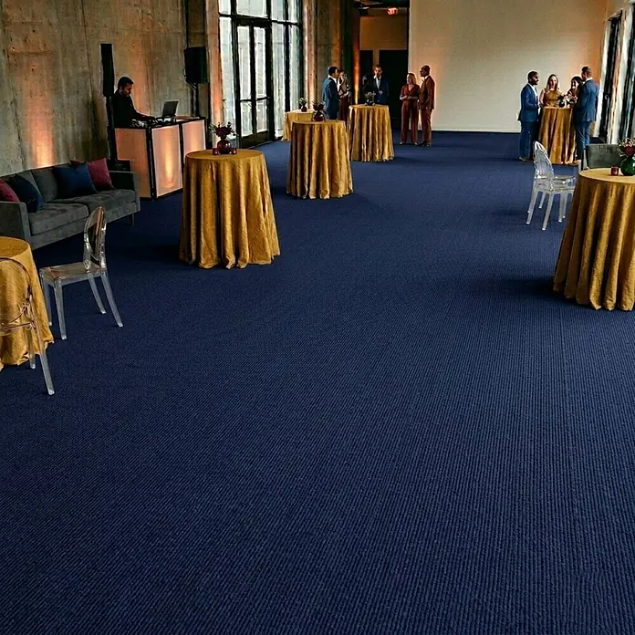 Floordirekt Teppichboden Meterware Sintra - für Messe & Events - Dunkelblau - 200 x 200 cm - Breite: 200 cm, Flachgewebe, Polypropylen, Dunkelblau - Blauer, texturierter Eventteppich bedeckt einen großen Boden mit Personen und Möbeln.