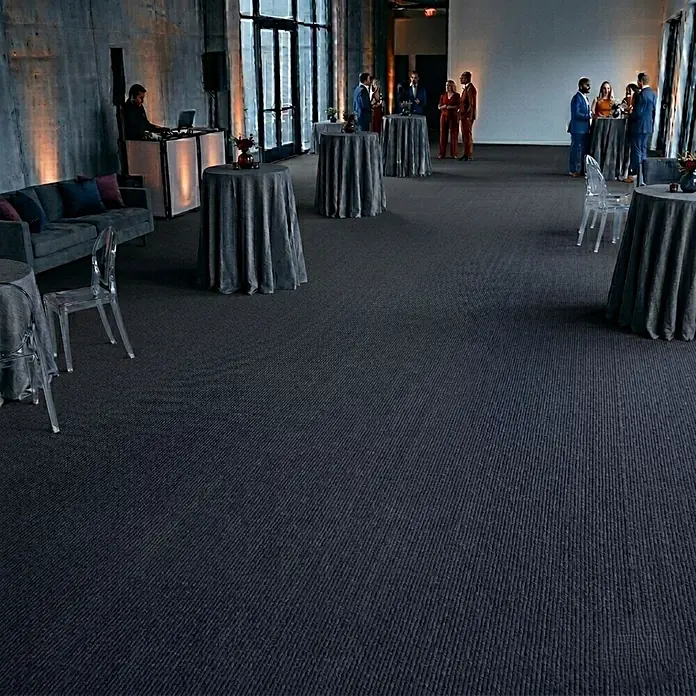Floordirekt Teppichboden Meterware Sintra - für Messe & Events - Dunkelgrau - 100 x 100 cm - Breite: 100 cm, Flachgewebe, Polypropylen, Dunkelgrau - Dunkelgrauer, gerippter Teppich in einem großen Veranstaltungsraum mit Gästen und Möbeln, der seine Textur und Nutzung zeigt.